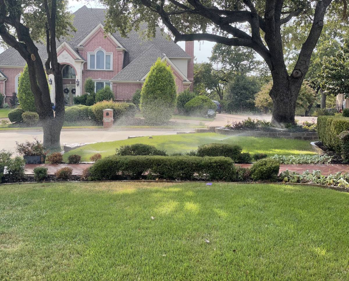 Sprinkler system running across a lawn and shrub beds in Grapevine, Texas during a repair visit