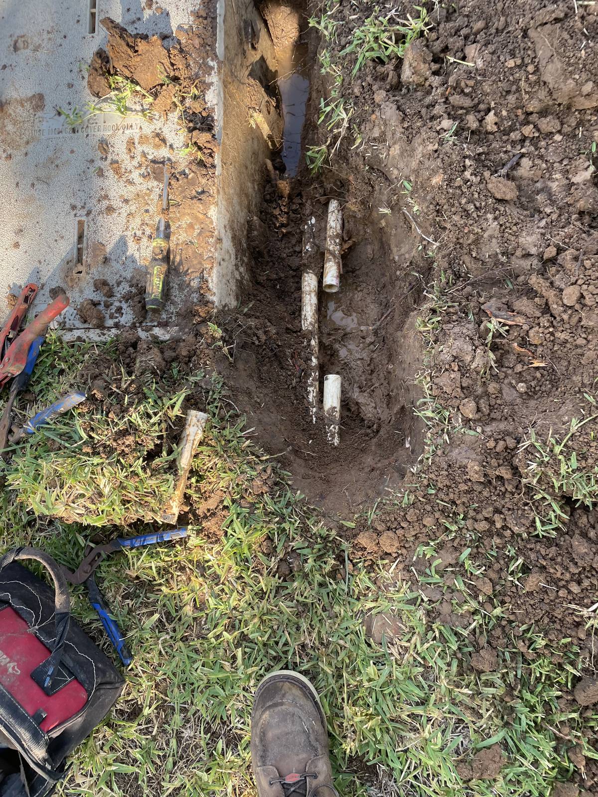 Exposed PVC sprinkler pipes in a muddy trench in North Richland Hills, Texas, with one section cut out for repair
